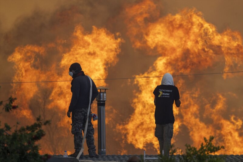 Residentes de la villa de Gennadi, en Grecia, observan sobre un tejado el avance de las llamas / Europa Press