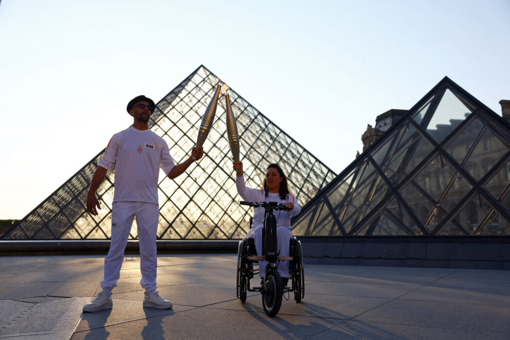 La antorcha olímpica en su llegada a París ha pasado por los lugares más emblemáticos de la ciudad. El cantante JR y la exesquiadora francesa Sandra Laoura durante el relevo de la antorcha olímpica en el Museo del Louvre / 14 de julio de 2024/ REUTERS / Stephanie Lecocq