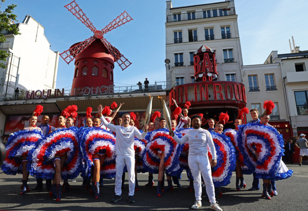 Tours de relevo de la antorcha París / 15 de julio de 2024 / Los portadores de la antorcha posan con la llama olímpica y los bailarines fuera del Moulin Rouge / REUTERS / Stephanie Lecocq