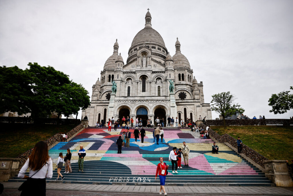 Los turistas se encuentran en las escaleras de la Basílica del Sacre-Coeur pintadas con el diseño de los Juegos Olímpicos y Paralímpicos de París 2024 en la Butte Montmartre en París, Francia / 3 de julio de 2024 / REUTERS / Yara Nardi