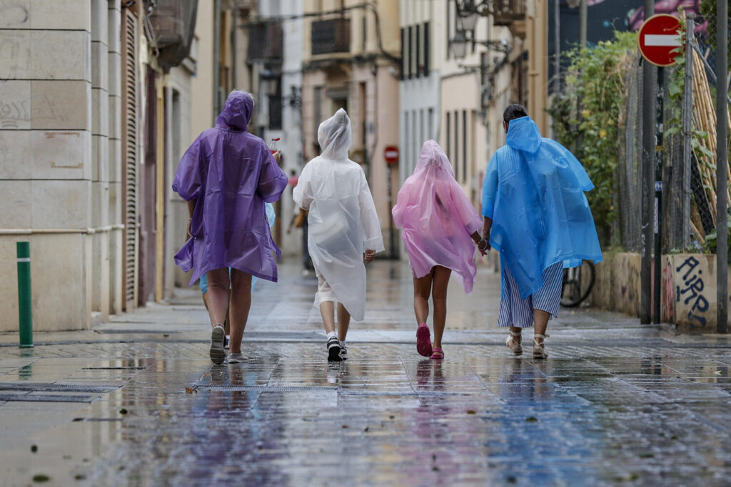 GRAFCVA2304. VALENCIA, 14/08/2024.- Varias personas caminan bajo la lluvia por una calle del centro de Valencia. La Aemet ha establecido el aviso naranja para este miércoles por tormentas con probable granizo y rachas muy fuertes de viento en toda la provincia de Alicante y en el sur de Valencia. EFE/Manuel Bruque