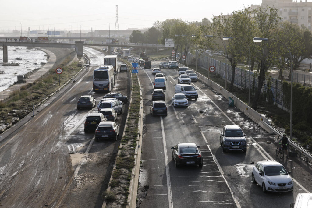 Varios coches circulan entre los vehículos afectados por la dana en la V30 a la altura de La Torre este viernes en Valencia. Los servicios de emergencia siguen trabajando en tareas de desescombro tras la devastadora dana que ha dejado al menos 95 fallecidos y que continuará en algunas zonas. EFE