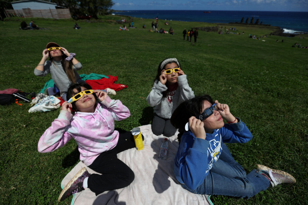 La gente observa el eclipse solar desde el área del monumento arqueológico de Tahai en el parque nacional Rapa Nui administrado por la comunidad nativa Mau Henua en la Isla de Pascua, Chile, 2 de octubre de 2024. REUTERS/Ivan Alvarado