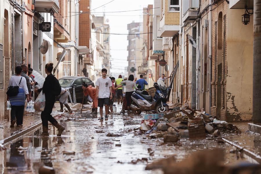 Unas personas caminan por una calle cubierta de lodo mientras otras se afanan en las labores de limpieza tras las intensas lluvias por la fuerte dana que afecta especialmente el sur y el este de la península ibérica, este miércoles en Valencia. EFE/Manuel Bruque