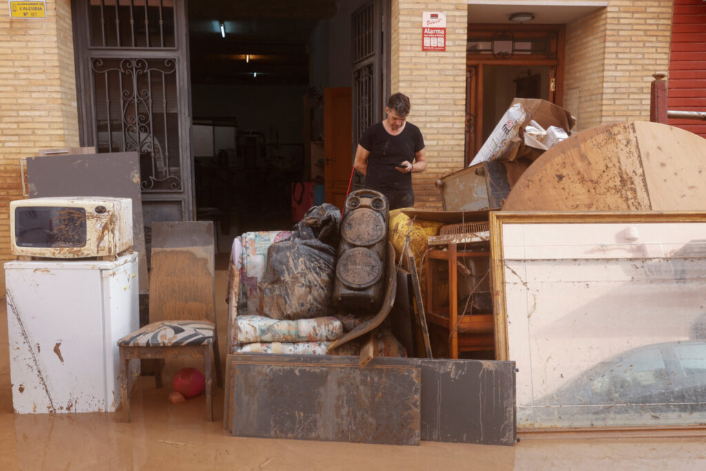 Un hombre revisa su teléfono mientras pertenencias personales dañadas se alinean en una calle cubierta de barro después de que las lluvias torrenciales causaron inundaciones en la Alcudia, región de Valencia, España, el 30 de octubre de 2024. REUTERS/Eva Manez