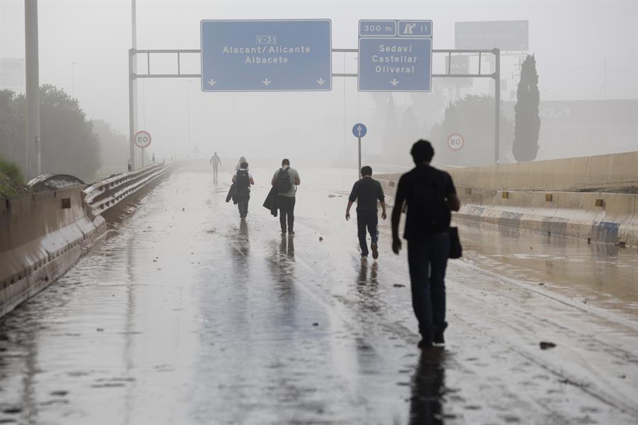 Varias personas transitan por la V-31 cerrada al tráfico a causa de las lluvias torrenciales de las últimas horas. EFE/Miguel Ángel Polo