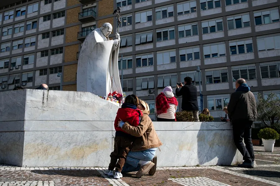 Varios fieles rezan por la salud del papa ante la estatua de Juan Pablo II situada en la entrada del hospital Gemelli de Roma. EFE/EPA/Angelo Carconi